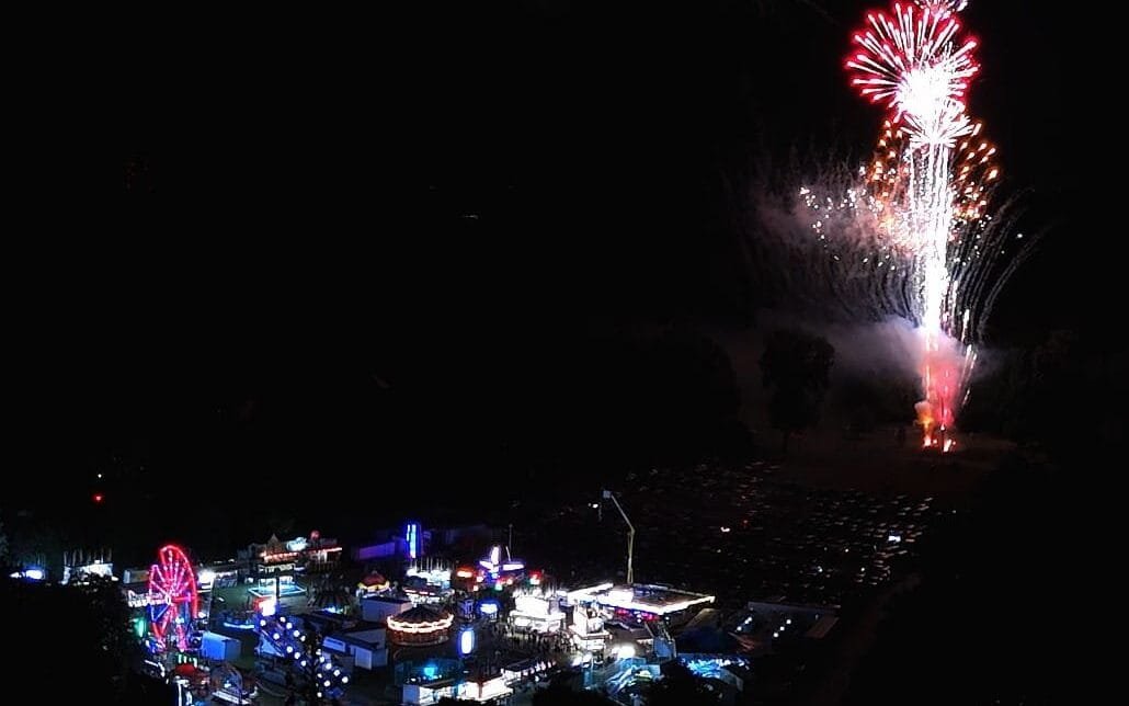 Black sky background with carnival lights at the bottom and fireworks near the right upper side.