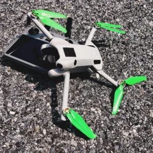 Gray drone with green blades on a rocky ground surface.